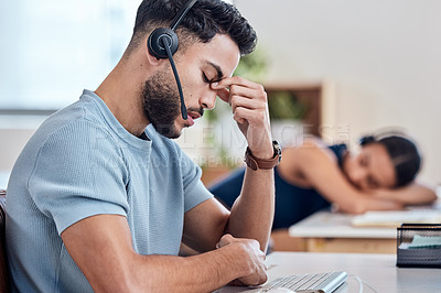 Buy stock photo Shot of a young male call center worker experiencing a headache while his coworker sleeps