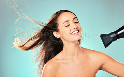 Buy stock photo Studio shot of an attractive young woman blowdrying her hair against a blue background