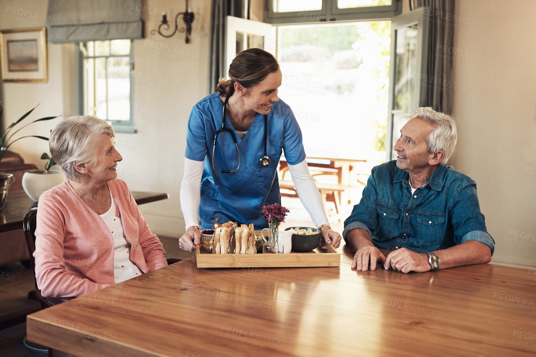 Buy stock photo Shot of a young nurse checking up on a senior couple during breakfast at a nursing home