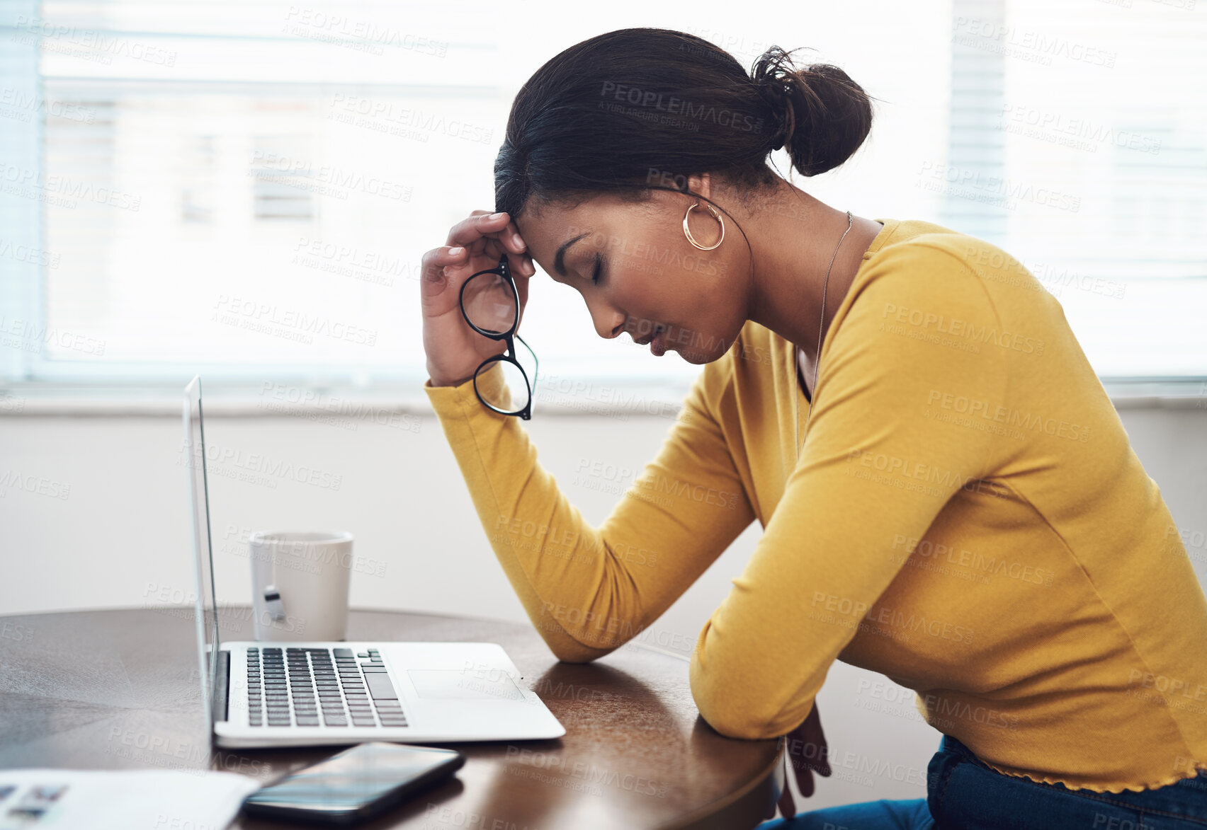 Buy stock photo Shot of an attractive young woman sitting alone at home and suffering from a headache while using her laptop