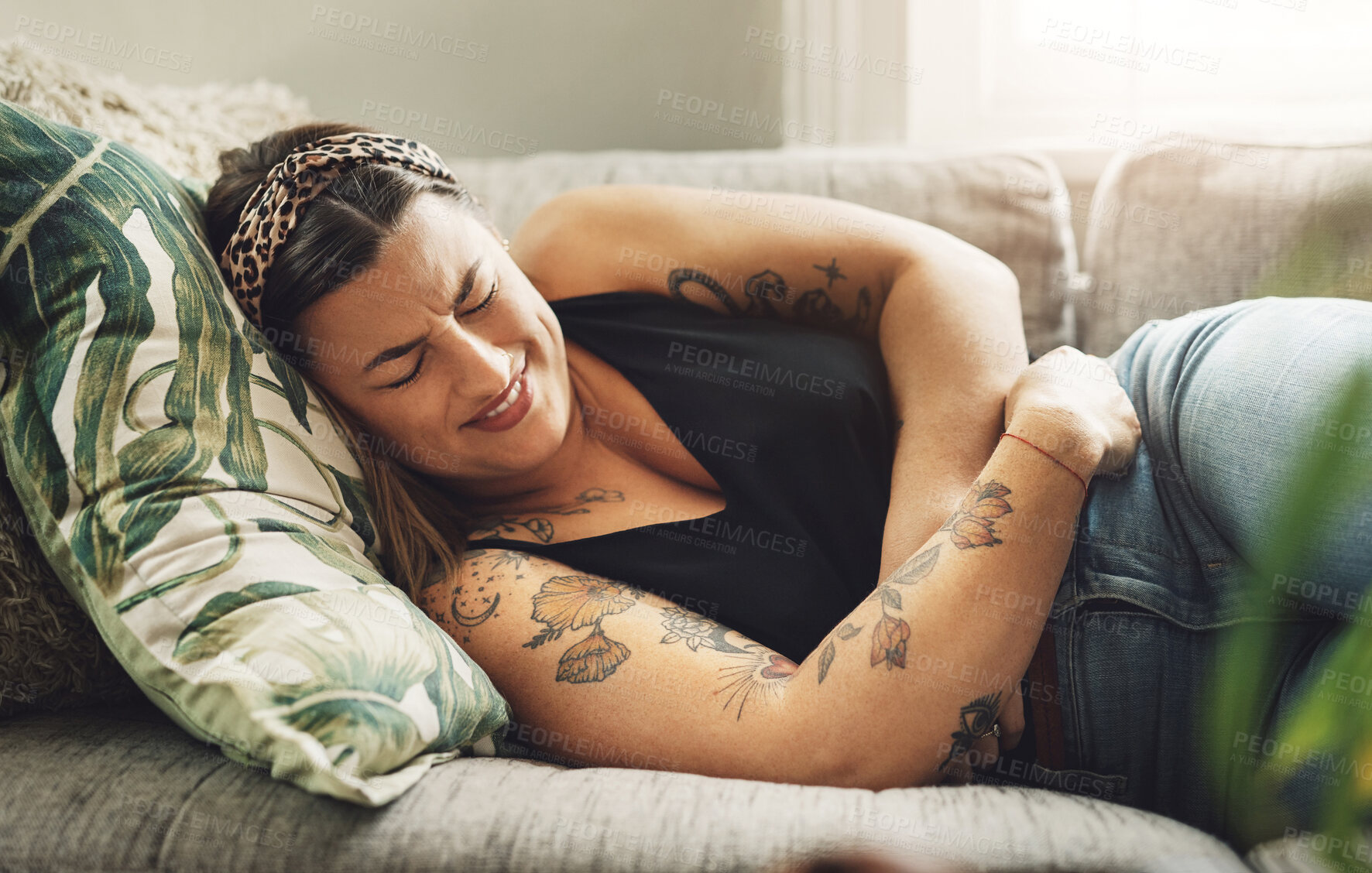 Buy stock photo Shot of a young woman experiencing stomach pain while lying on the sofa at home