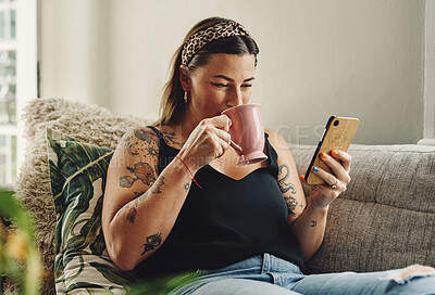 Buy stock photo Shot of a young woman using a smartphone and having coffee on the sofa at home