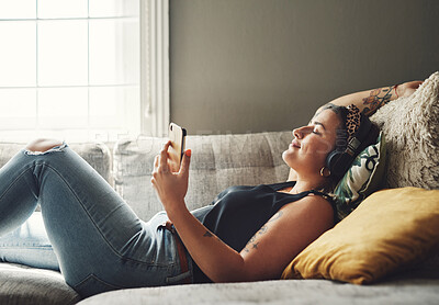 Buy stock photo Shot of a young woman using headphones and a smartphone on the sofa at home