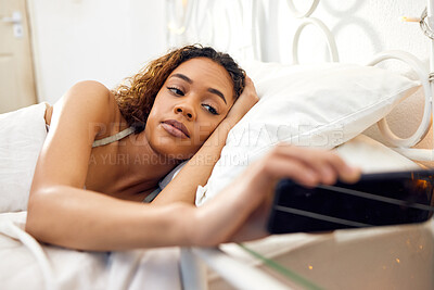 Buy stock photo Shot of an attractive young woman lying in her bed in the morning at home and checking her cellphone