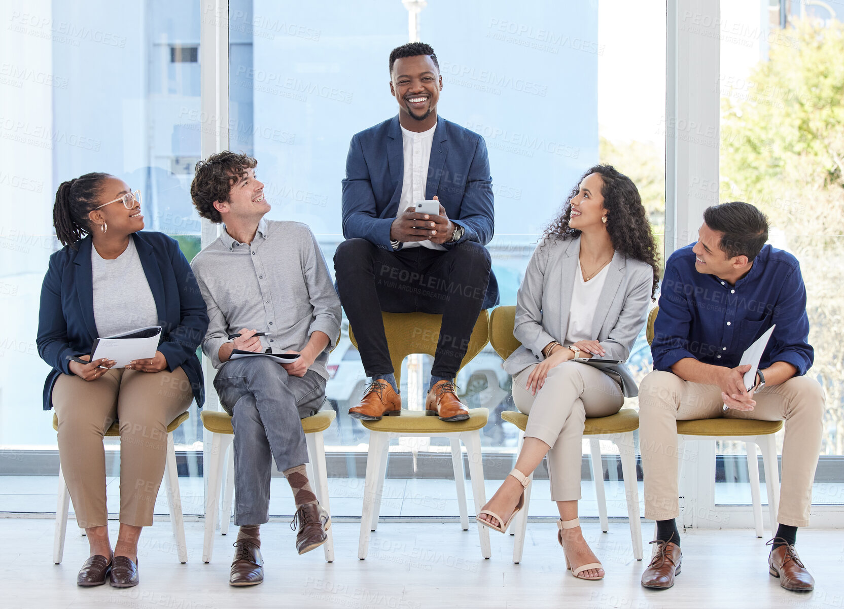 Buy stock photo Portrait of a young businessman sitting on a chair alongside candidates in an office