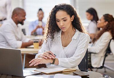 Buy stock photo Shot of a young businesswoman checking the time while working on a laptop in an office with her colleagues in the background