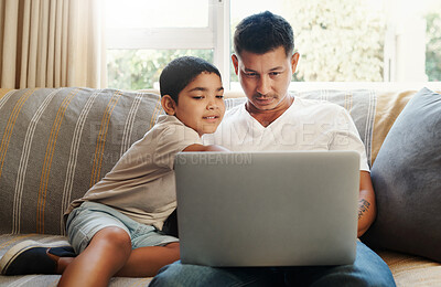 Buy stock photo Shot of a handsome young man sitting on the sofa and bonding with his son while using a laptop
