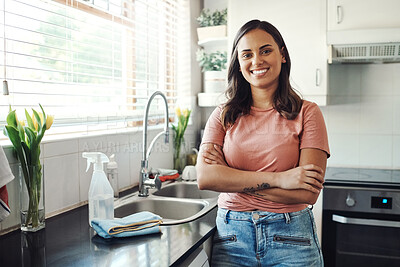 Buy stock photo Shot of an attractive young woman standing alone with her arms folded in her kitchen at home