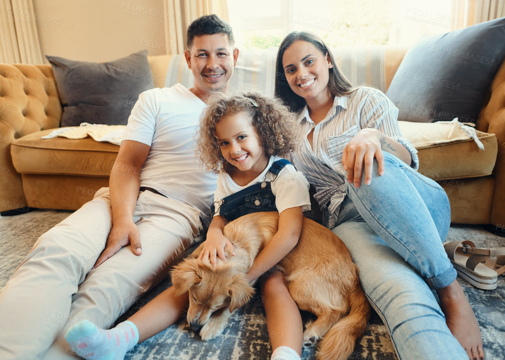 Buy stock photo Shot of a young family sitting on the floor in the living room at home and bonding with their dog