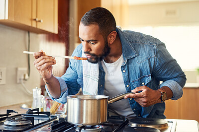 Buy stock photo Shot of a man using a wooden spoon to taste his food while cooking