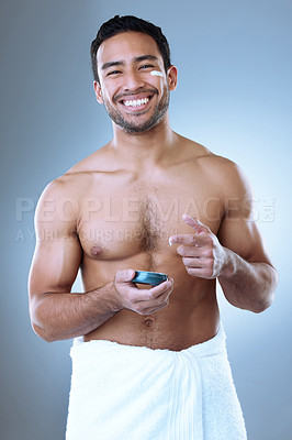 Buy stock photo Studio portrait of a young man happily applying moisturiser to his face against a grey background