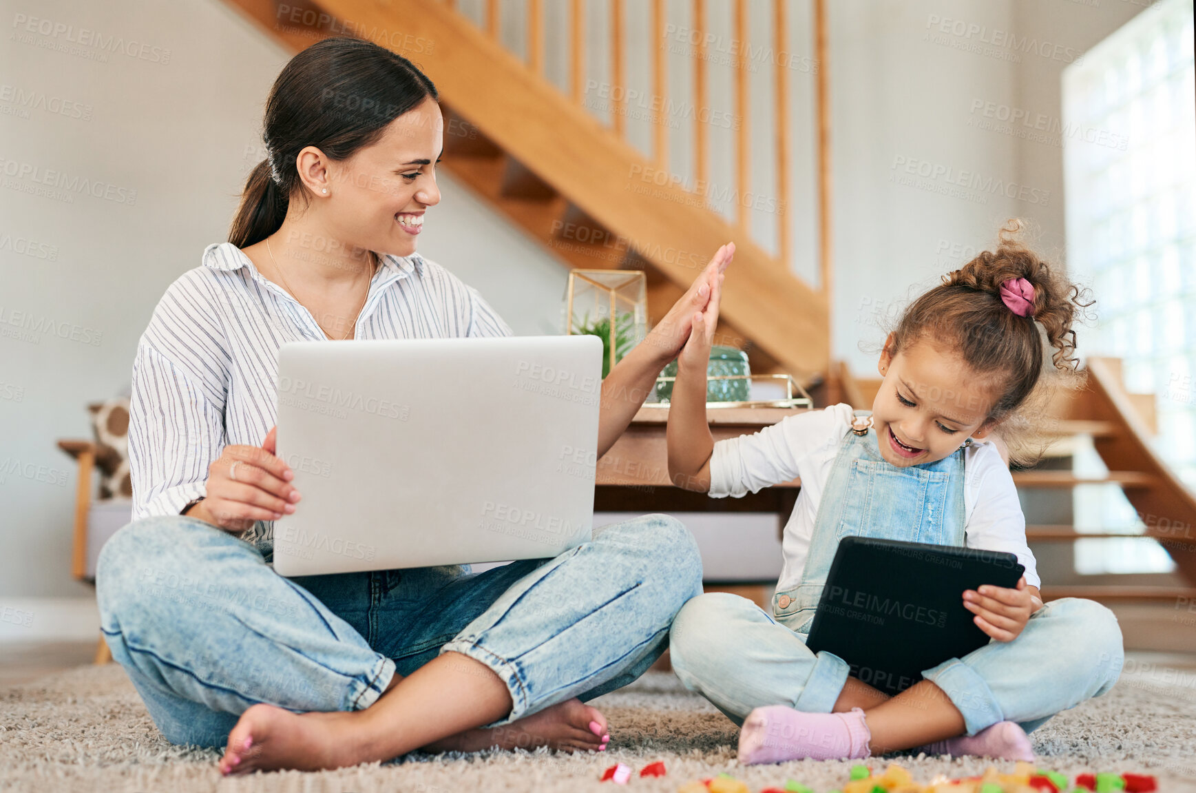 Buy stock photo Shot of a mother and her little daughter giving each other a high five while using digital devices at home