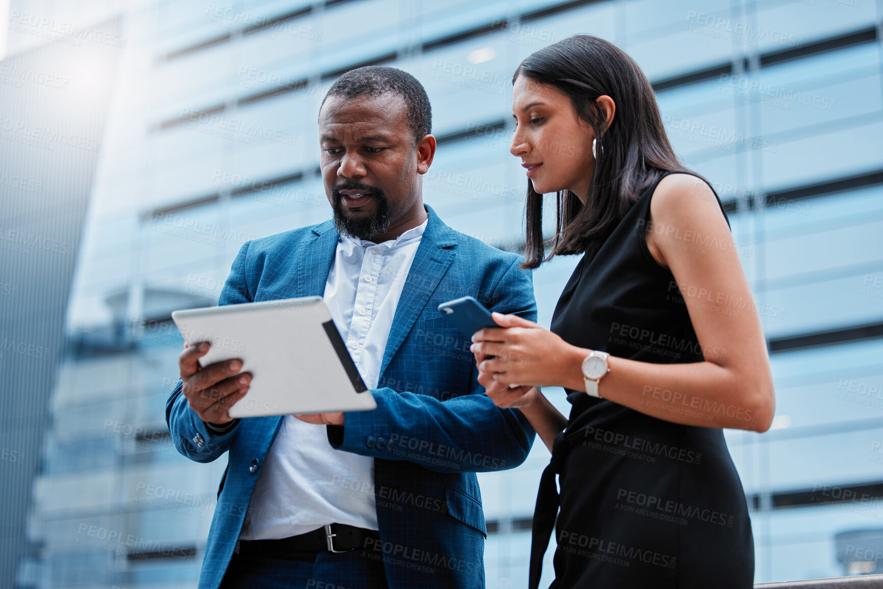 Buy stock photo Low angle shot of a handsome mature businessman showing a female colleague something on his tablet while standing outside on the office balcony