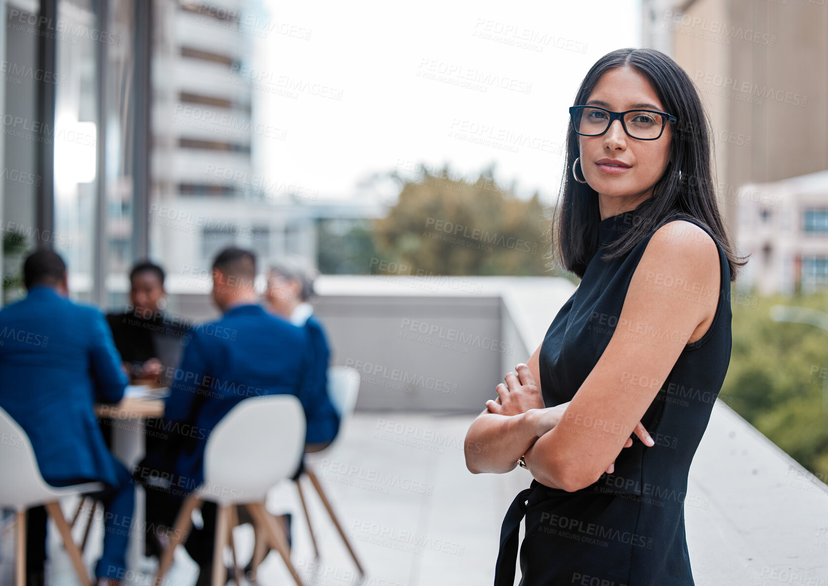 Buy stock photo Cropped portrait of an attractive young businesswoman standing with her arms folded outside on the office balcony with her colleagues in the background