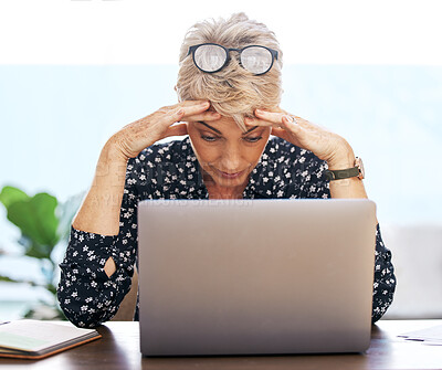 Buy stock photo Shot of a mature woman sitting alone and feeling stressed while using her laptop to work from home