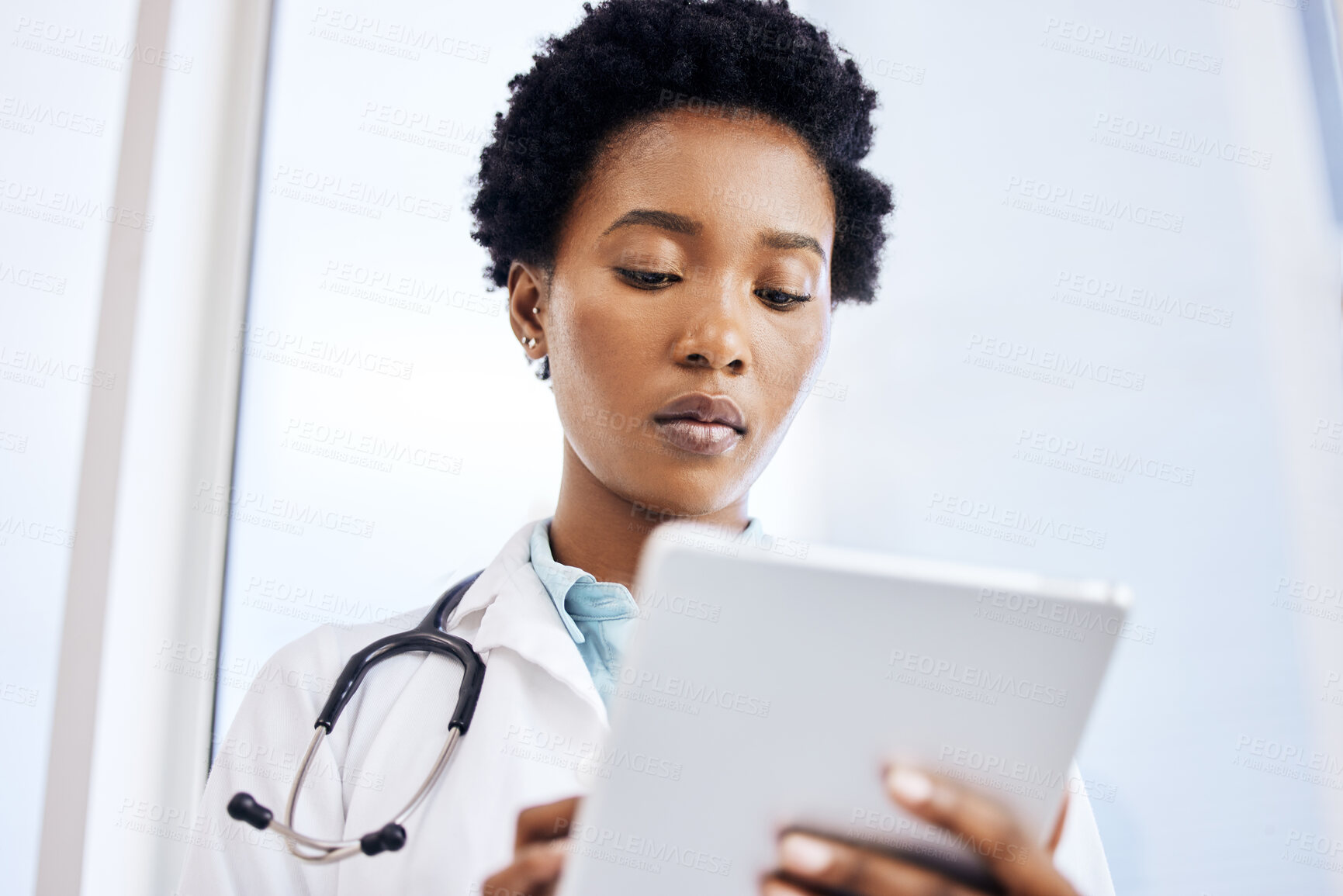 Buy stock photo Low angle shot of an attractive young female doctor using her tablet while standing in the office