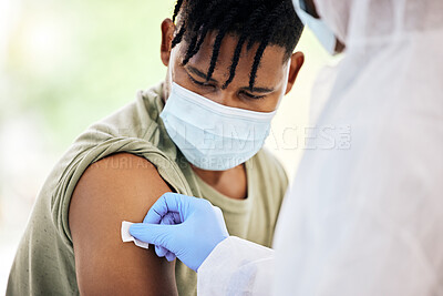 Buy stock photo Cropped shot of an unrecognizable doctor cleaning the injection site of a handsome young male patient before administering the covid 19 vaccine