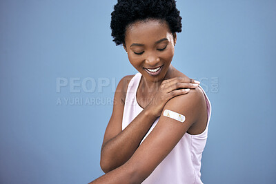 Buy stock photo Black woman, happy and vaccine plaster in studio for prevention, health and covid 19 on blue background. Vaccinated, smile and female person with pride for wellness, healthcare and medical injection