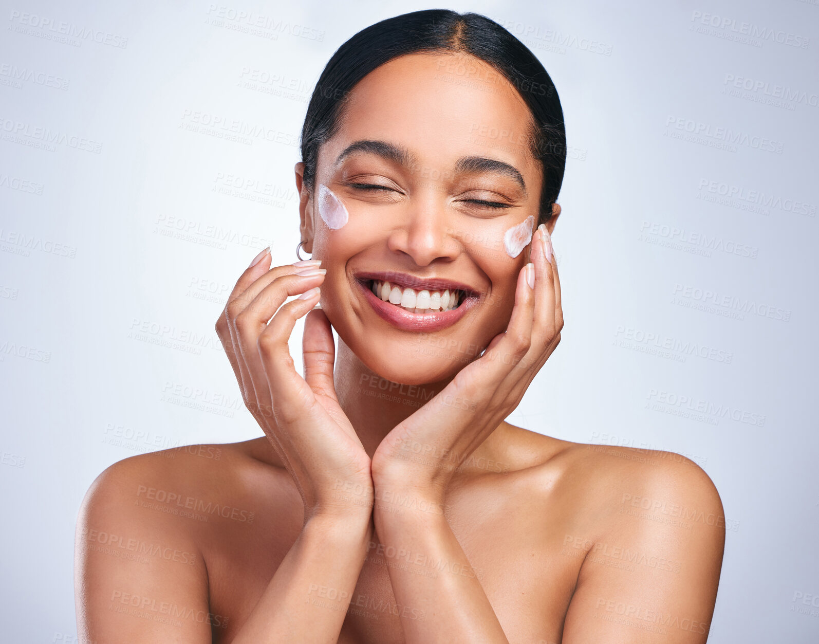 Buy stock photo Shot of an attractive young woman applying moisturiser against a grey background