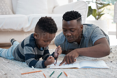 Buy stock photo Shot of a young father lying on the the living room floor and helping his son draw