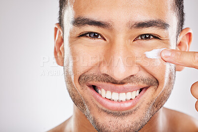 Buy stock photo Closeup studio portrait of a young man happily applying moisturiser to his face against a grey background