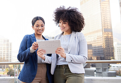 Buy stock photo Shot of two young businesswomen standing outside on the balcony and using a digital tablet