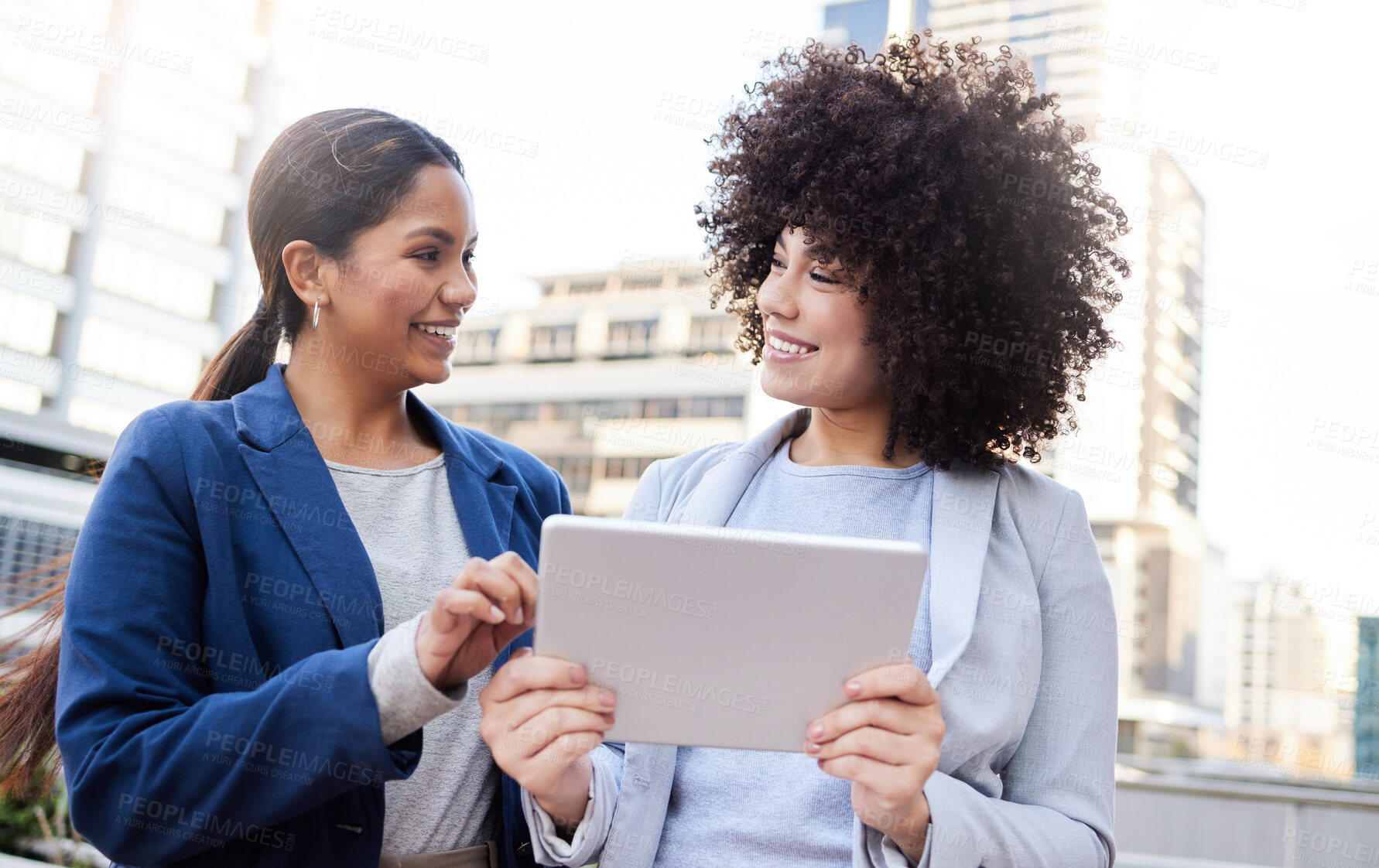 Buy stock photo Shot of two young businesswomen standing outside on the balcony and using a digital tablet