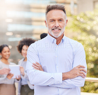 Buy stock photo Shot of a handsome mature businessman standing outside with his arms folded while his colleagues discuss behind him