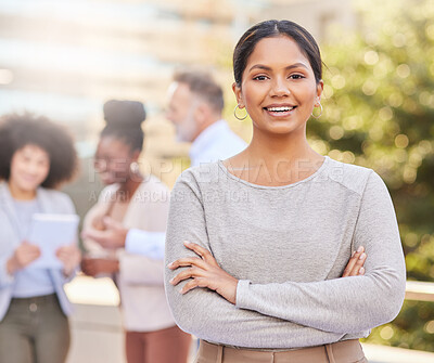 Buy stock photo Shot of an attractive young businesswoman standing outside with her arms folded while her colleagues discuss behind her