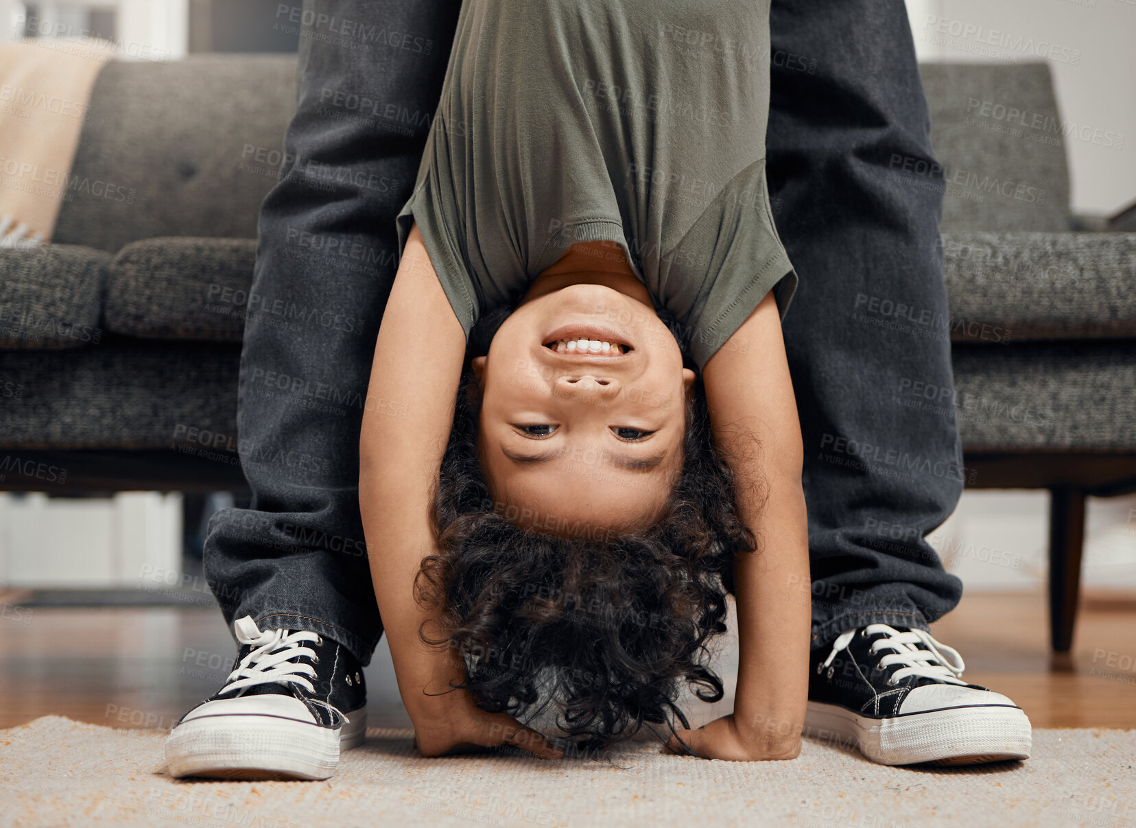 Buy stock photo Playful young boy being held upside down while having fun and playing with his father at home. Closeup portrait of the head and face of a cute little male child doing a handstand with his single dad