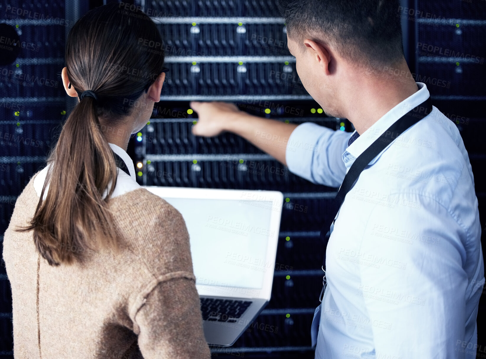 Buy stock photo Rearview shot of two technicians working together in a sever room