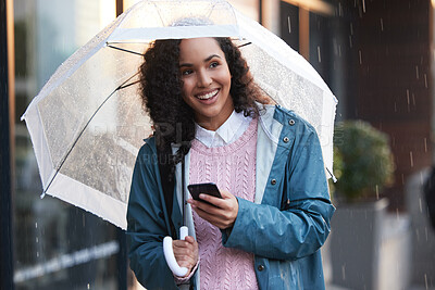 Buy stock photo Shot of a young woman using a phone while holding an umbrella in the city