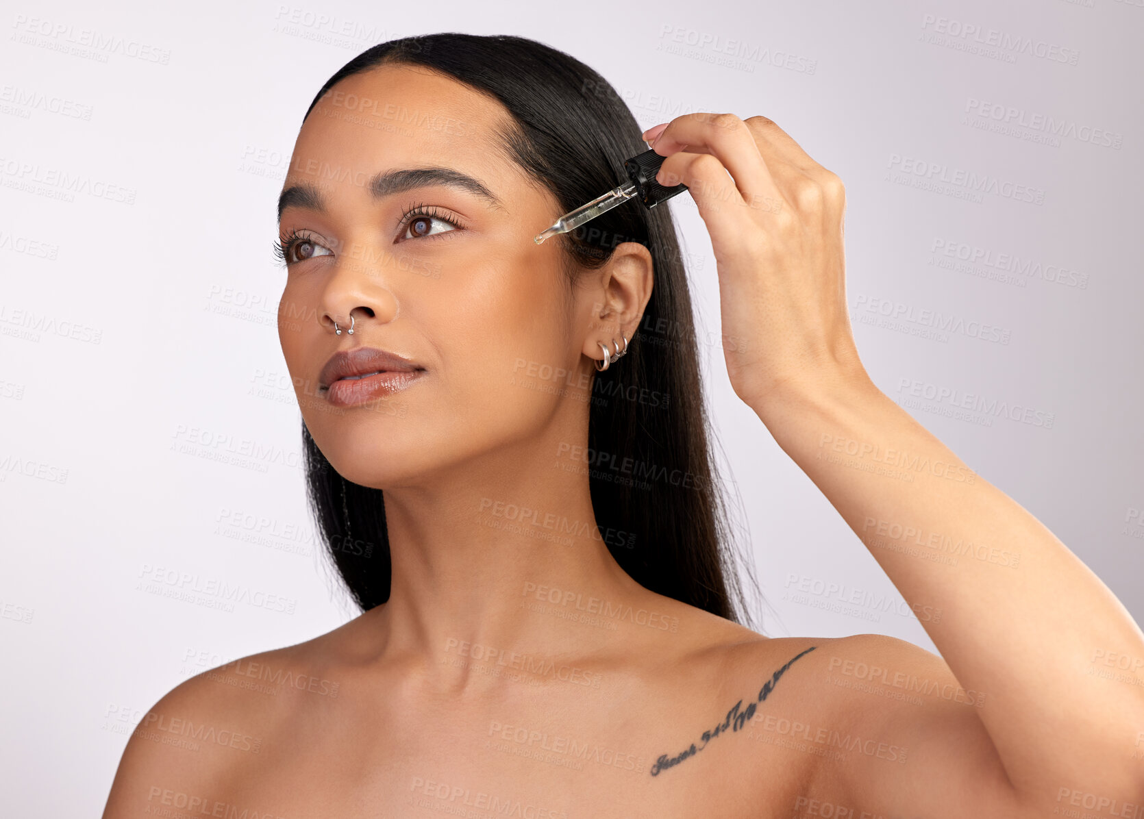 Buy stock photo Studio shot of an attractive young woman using a dropper to apply beauty serum to her face against a pink background