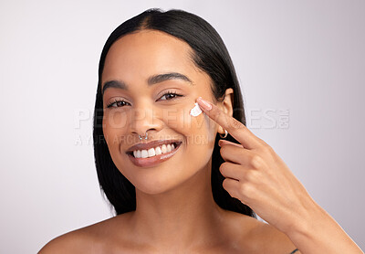 Buy stock photo Studio portrait of an attractive young woman applying moisturizer to her face against a pink background