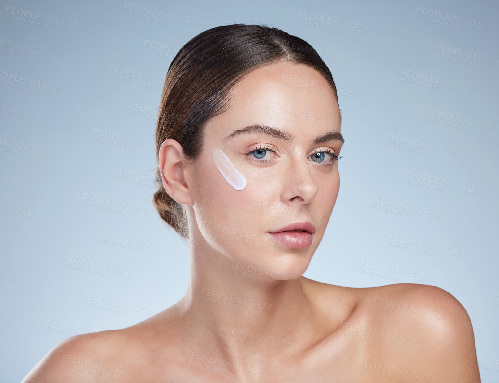 Buy stock photo Studio portrait of an attractive young woman moisturizing her face against a grey background