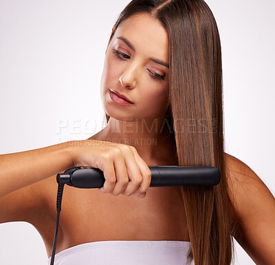 Buy stock photo Studio shot of an attractive young woman straightening her hair against a grey background