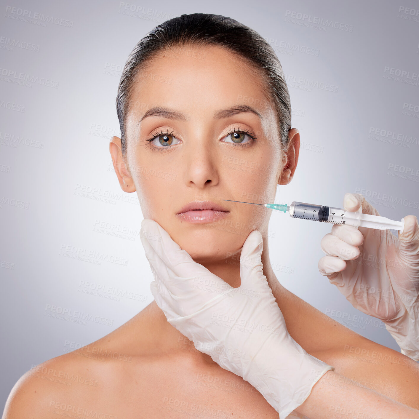 Buy stock photo Shot of a beautiful young woman getting her face injected by gloved hands against a grey background
