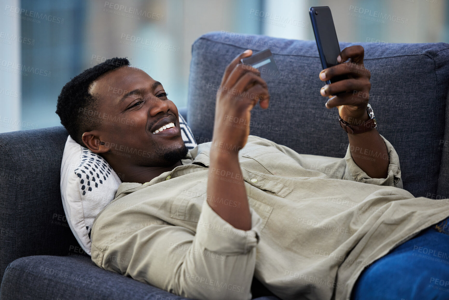 Buy stock photo Shot of a young man using a credit card and phone on the couch at home