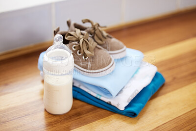 Buy stock photo Home, baby clothes and shoes with milk, prepare for toddler and calcium on wooden table. Empty, sneakers and nutrition with fashion for child, dairy and fresh with folded laundry in house with bottle