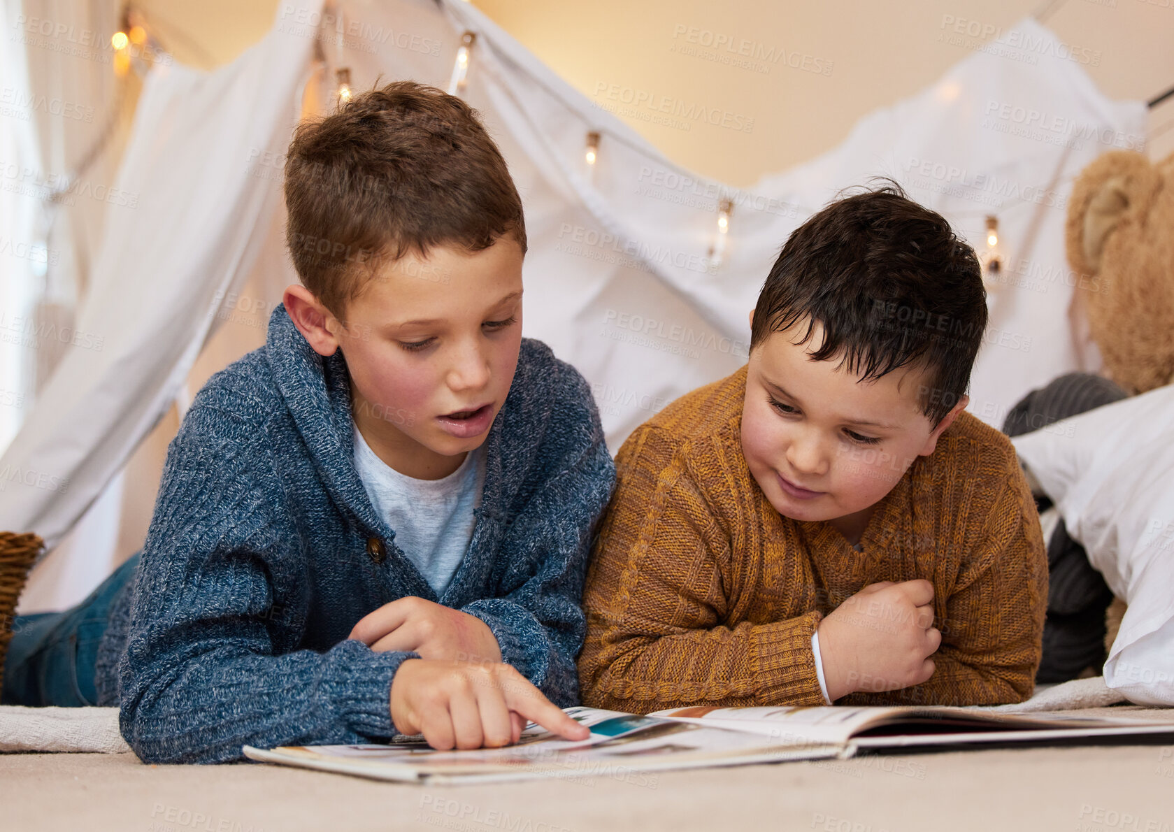 Buy stock photo Shot of two brothers reading a book together under a blanket fort at home