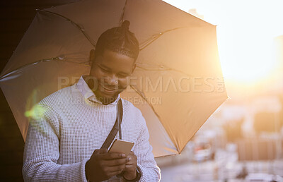 Buy stock photo Shot of a young businessman using a cellphone while holding an umbrella on a rainy day in the city