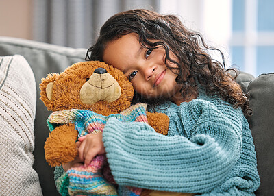 Buy stock photo Shot of an adorable little girl sitting alone on the sofa at home and holding a teddy bear