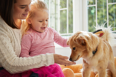 Buy stock photo Shot of a little girl sitting on her mother's lap while brushing their puppy