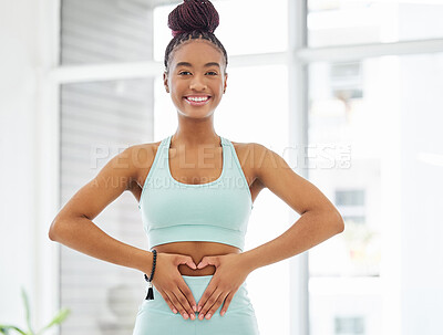 Buy stock photo Shot of a young woman standing alone in the yoga studio and making a heart shaped gesture over her stomach
