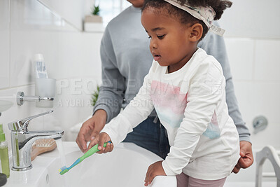 Buy stock photo Shot of a mother helping her little daughter rinse her toothbrush at a tap in the bathroom at home