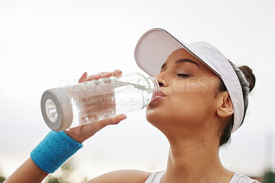 Buy stock photo Shot of a beautiful young woman drinking a bottle of water while out playing tennis