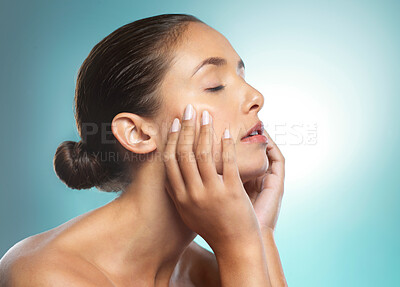 Buy stock photo Shot of a young female touching a her soft skin against a blue background