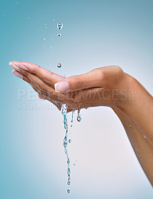 Buy stock photo Cropped shot of an unrecognisable woman cupping her hands to catch water against a blue background in the studio