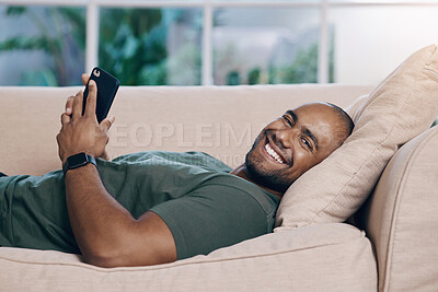 Buy stock photo Shot of a young man relaxing on his couch using his smartphone to send a text