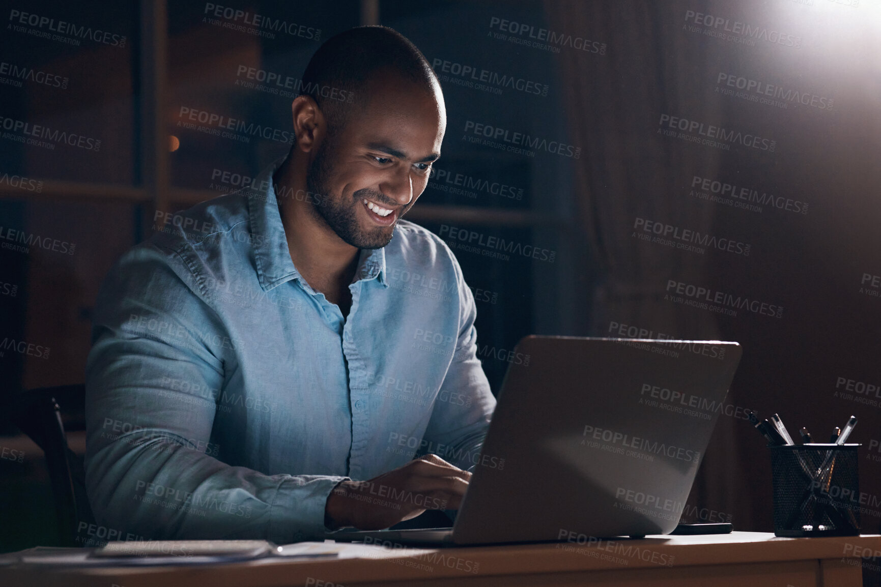 Buy stock photo Shot of a young businessman using his laptop while working late at night
